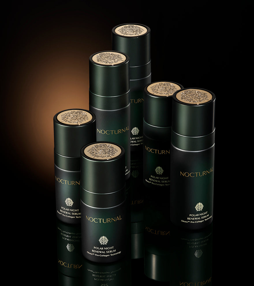 six skincare serum bottles sitting next to each other. the serum bottles are dark green, frosted glass. there is a nice golden glow surrounding the skincare bottles.