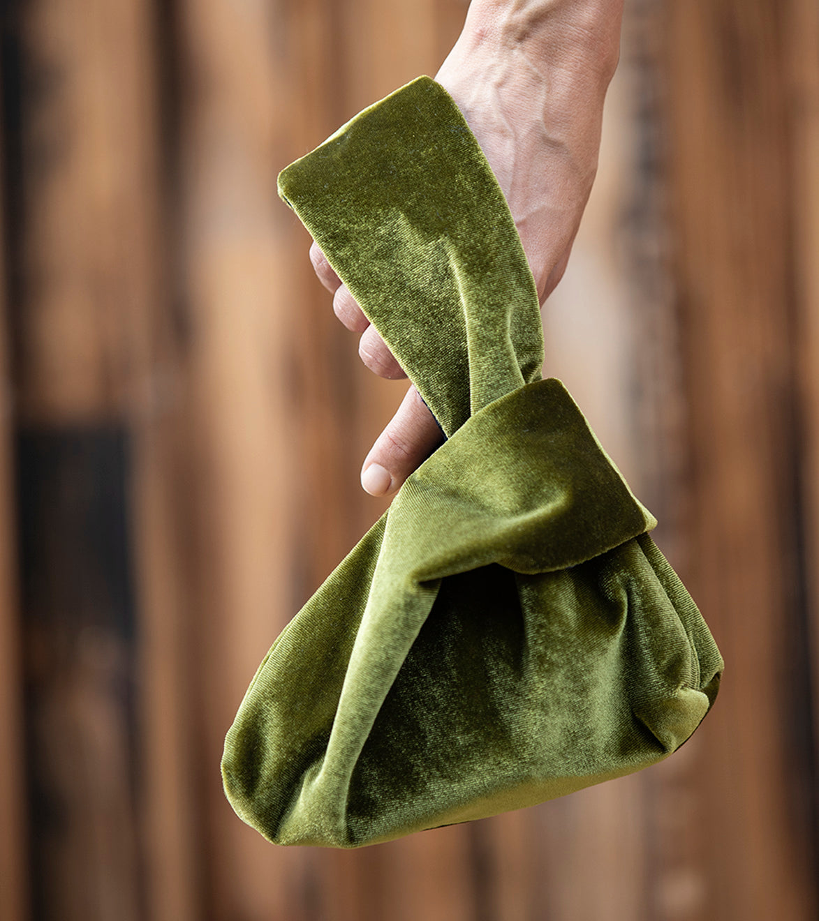 Image of a model holding the Japandi Japanese knot bag. It is an olive green bag made out of Scandinavian velvet. 